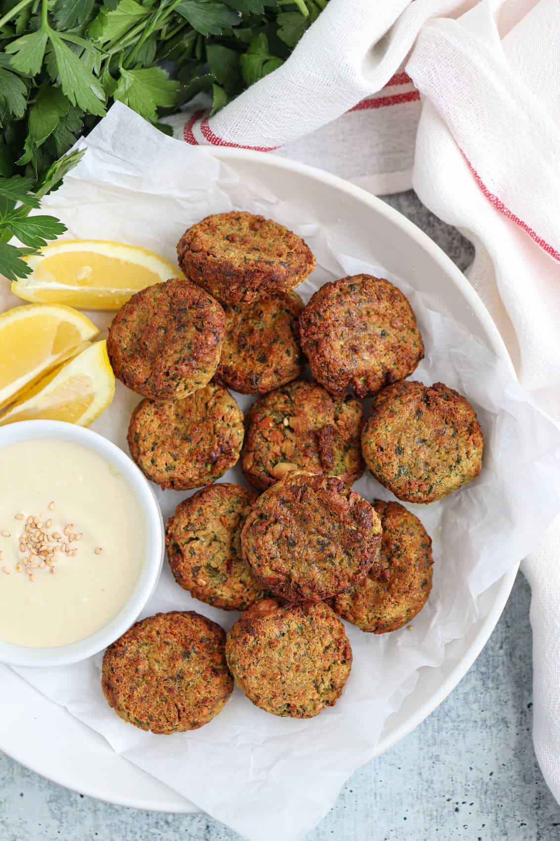 air fried falafel patties on a paper lined place with a side of tahini sauce and lemon wedges.