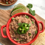 refried beans in a red pot with jalapeno on top.