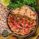 pinto beans and rice in a round brown bowl topped with pico de gallo.