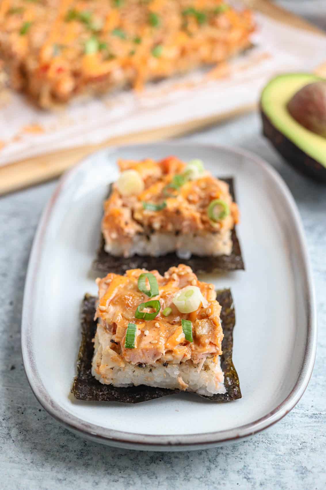 two salmon sushi bake with rice served on small nori sheets on a small gray rectangular plate. 
