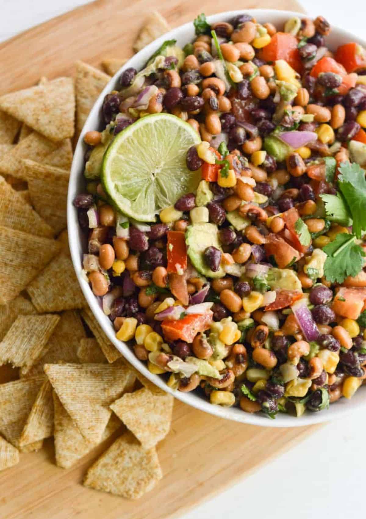 bean salad in a white bowl surrounded by corn chips.