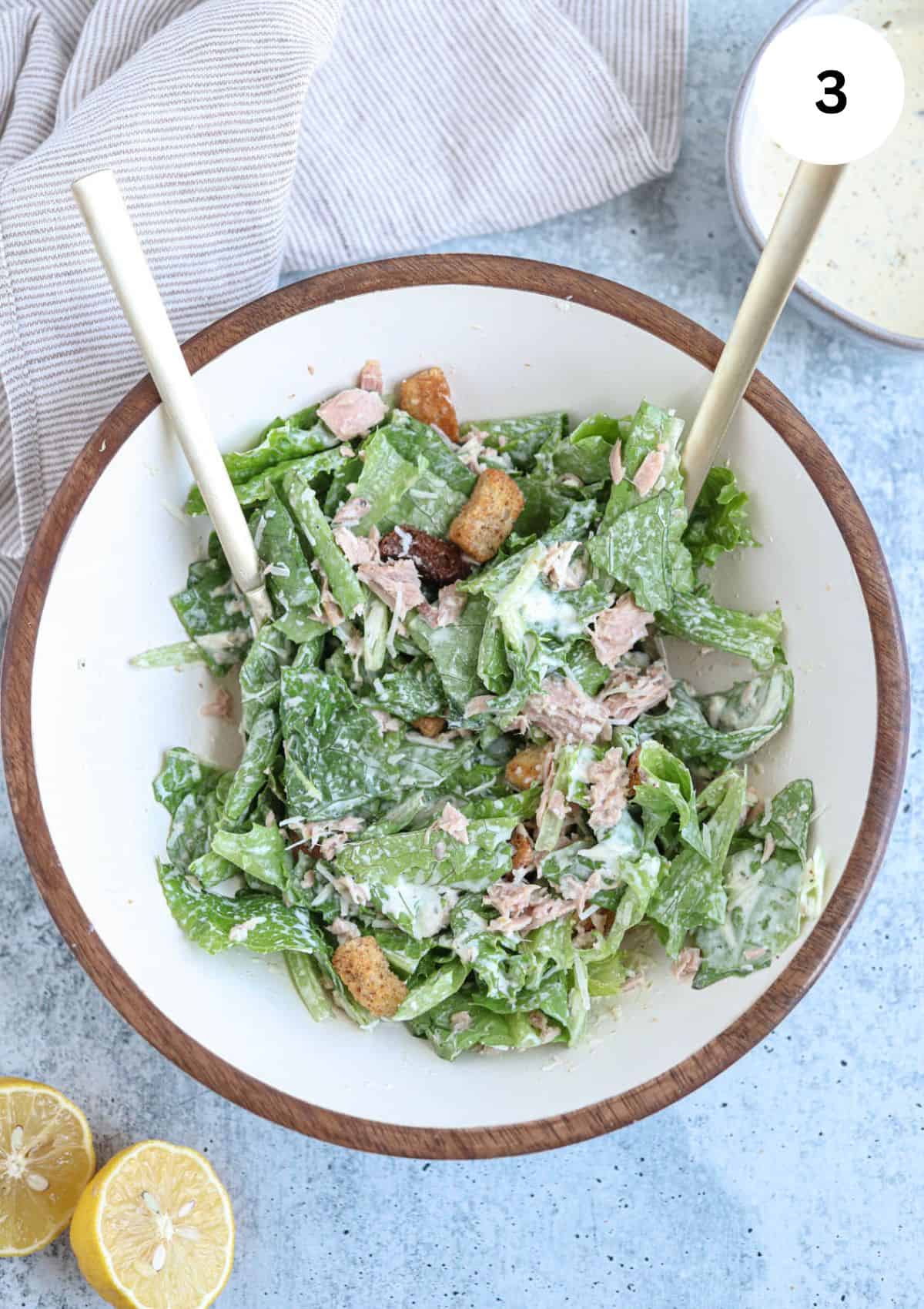 caesar salad wth coutons , tuna, parmesan cheese and dressing in a  bowl.
