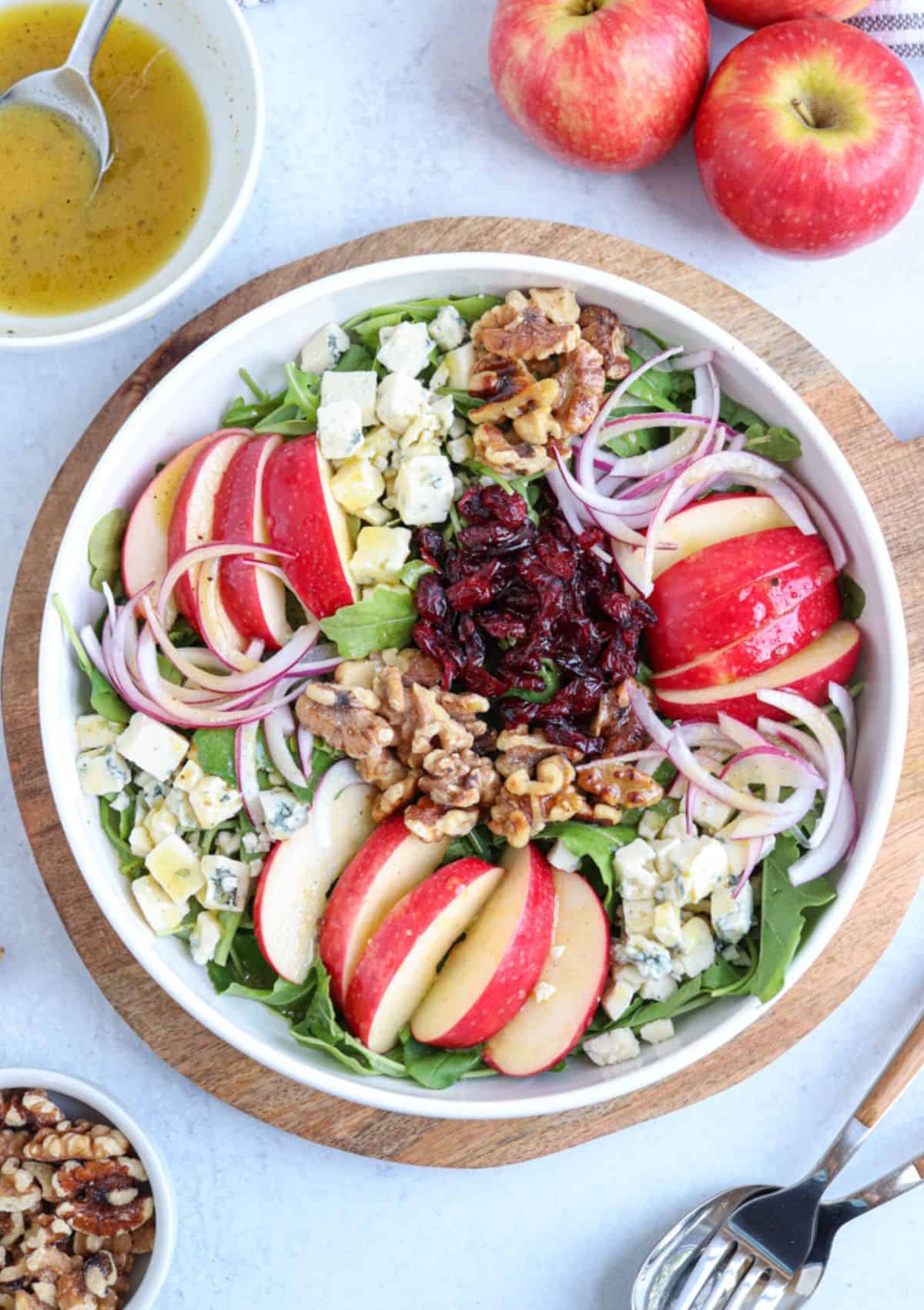 salad with sliced apples and gorgonzola in a white bowl on a wooden board.
