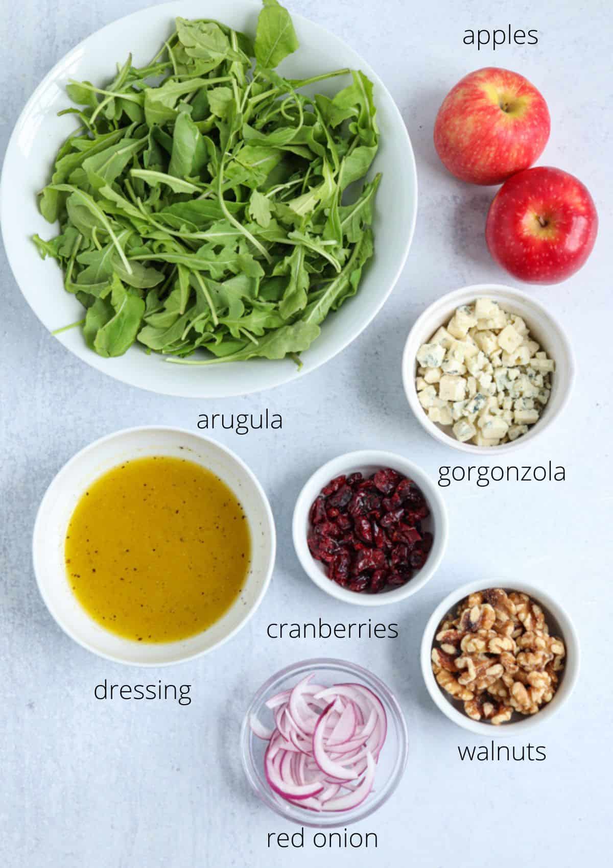 ingredients for making apple gorgonzola salad in small containers on light gray background.