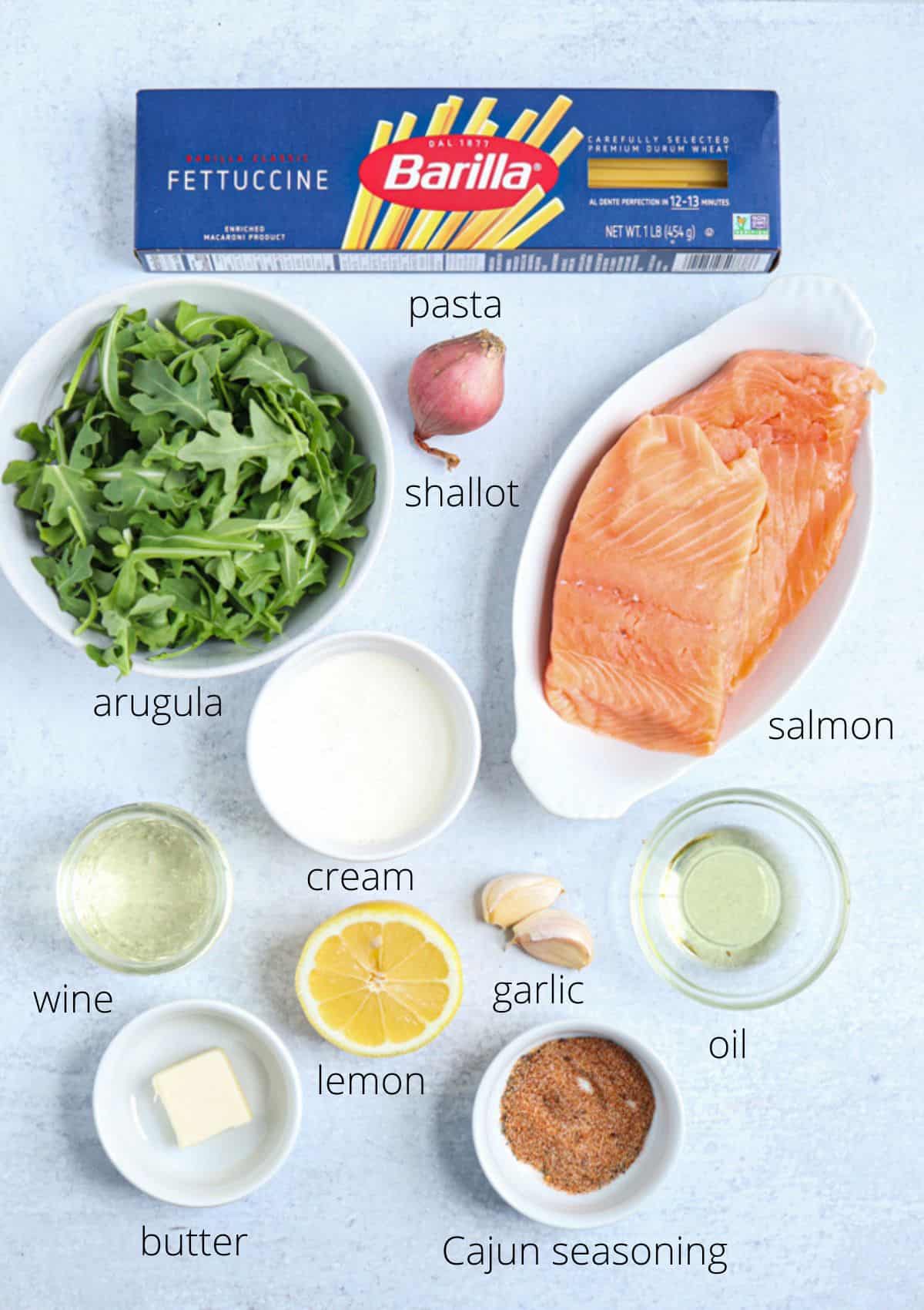 ingredients for making Cajun salmon pasta on light gray background.