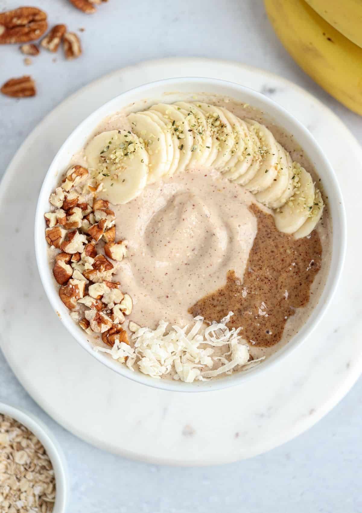 oatmeal smoothie bowl topped with sliced banana, chopped pecans, coconut flakes and almond butter.