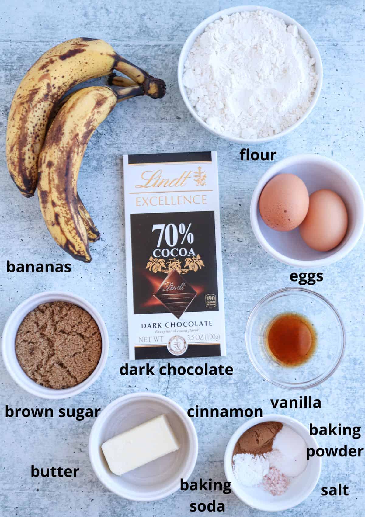 A delightful array for banana bread awaits on the surface: ripe bananas, a touch of dark chocolate, flour, eggs, brown sugar, butter, cinnamon, vanilla, baking soda, baking powder, salt—and with a savory falafel platter nearby for a perfect sweet and savory balance.