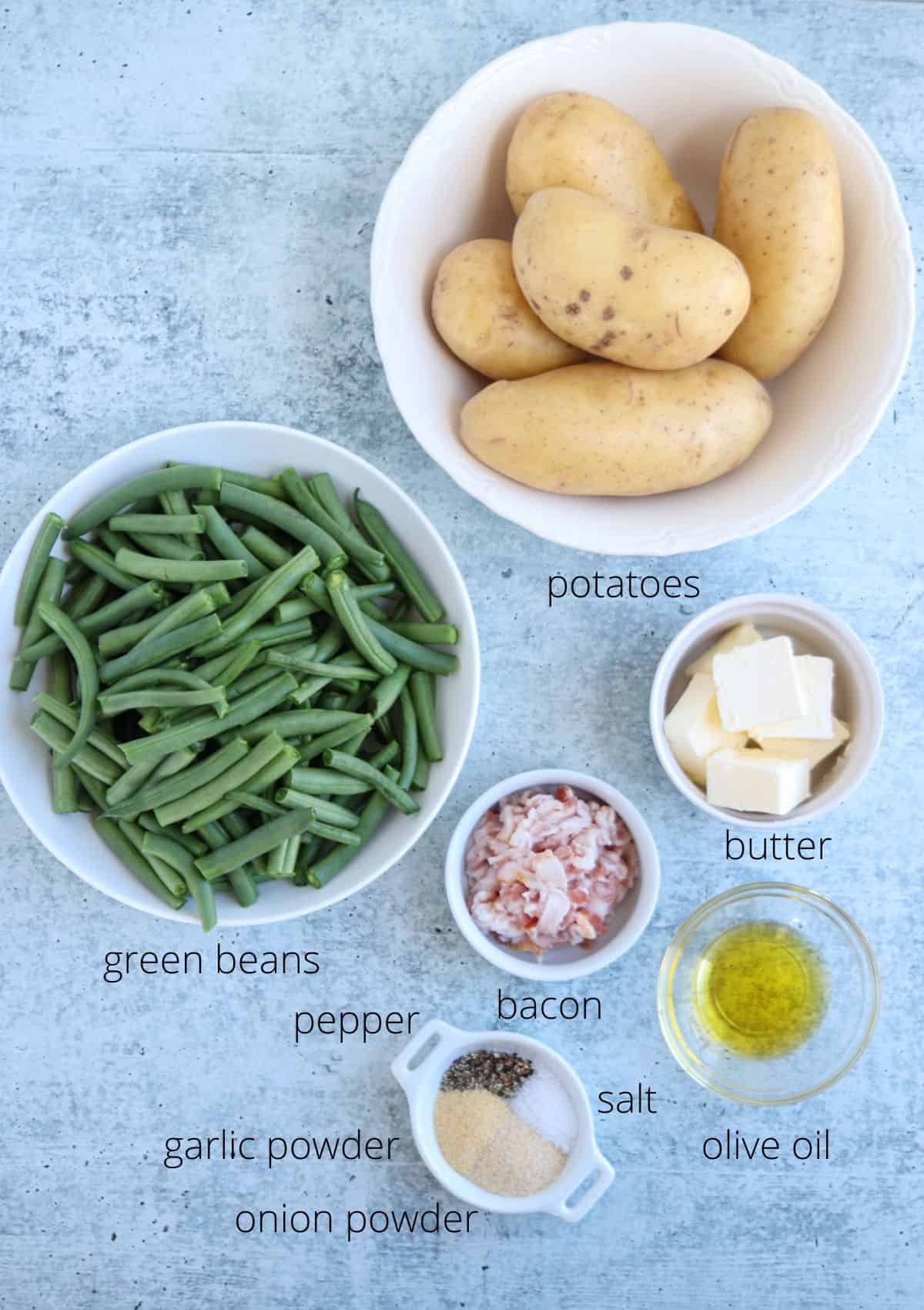 A flat lay of ingredients—including whole potatoes, chopped green beans, diced bacon, cubes of butter, olive oil, salt, pepper, garlic powder, and onion powder—perfect for a hearty chicken potato broccoli casserole.