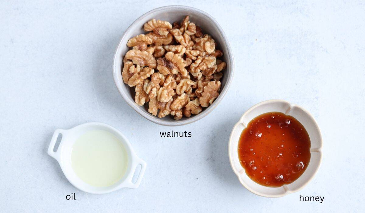 A bowl of walnut halves, a small dish of oil, and a small bowl of honey are arranged on a light surface, each labeled with text—perfect ingredients to complement a chicken potato broccoli casserole.