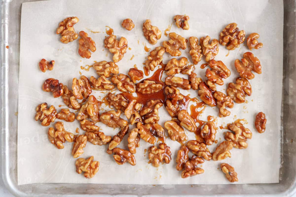 Caramelized walnuts spread out on parchment paper, resting on a baking tray with a glossy coating and some caramel pooling around the nuts—perfect as a crunchy topping for your favorite chicken potato broccoli casserole.