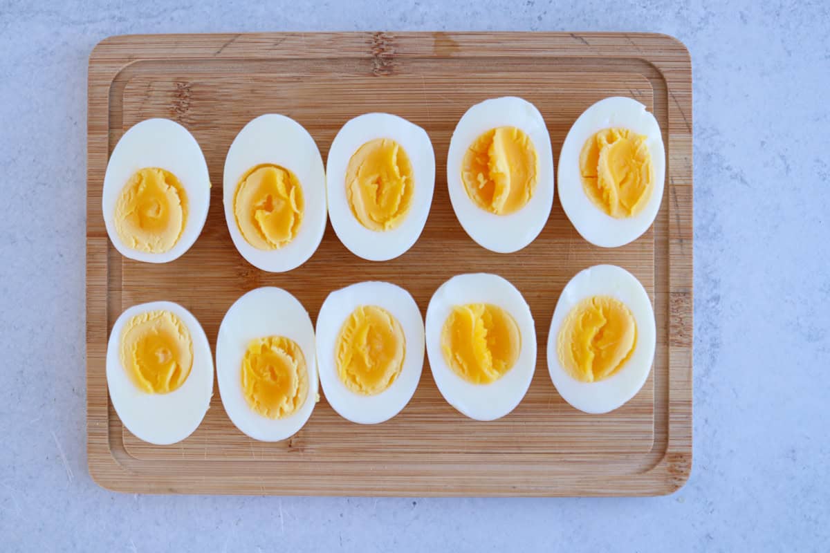 Ten hard-boiled egg halves arranged in two rows on a wooden cutting board, their yellow yolks and firm whites.