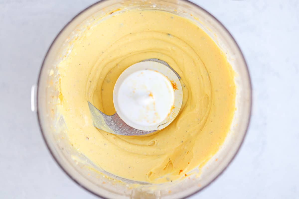 Overhead view of a food processor bowl filled with a smooth, creamy yellow-orange mixture.