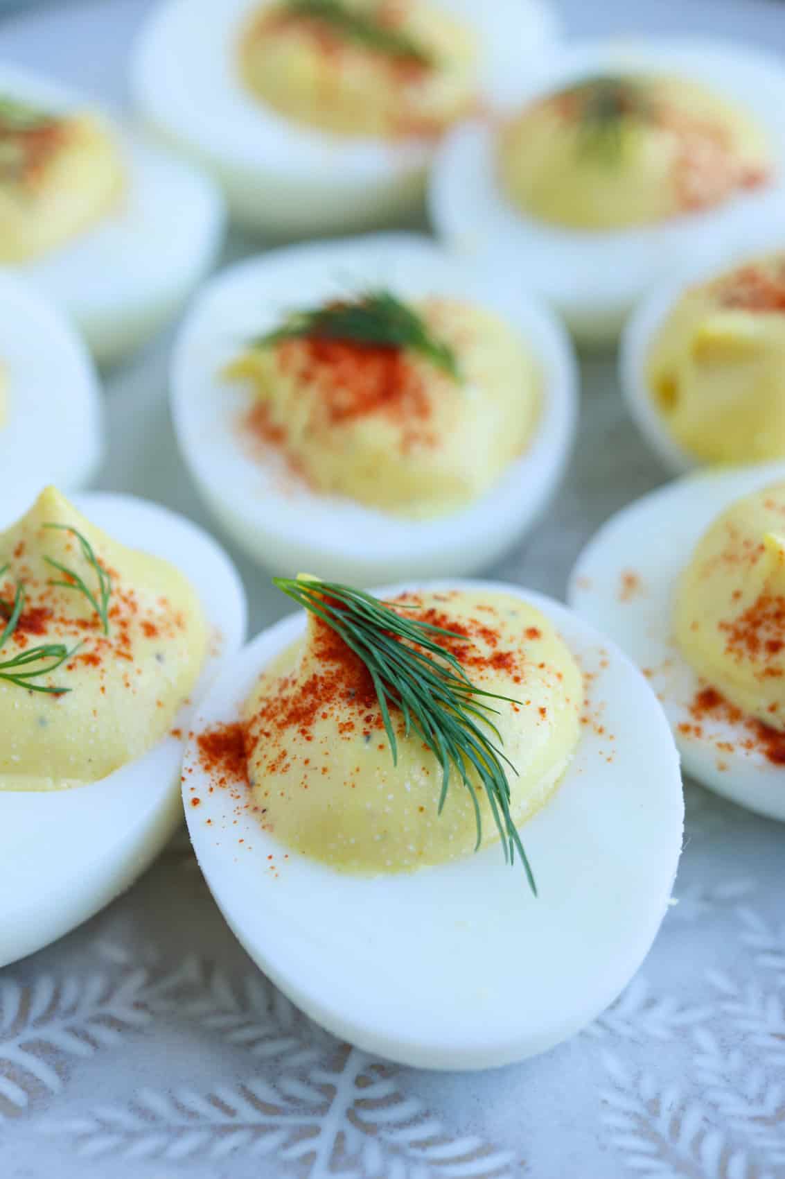 Close-up of deviled eggs topped with paprika and fresh dill, arranged on a light-colored patterned plate—a perfect appetizer.