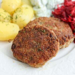 Two browned kotlety mielone (Polish meat patties) are served on a white plate with boiled potatoes topped with dill, shredded beets, and a creamy salad in the background.