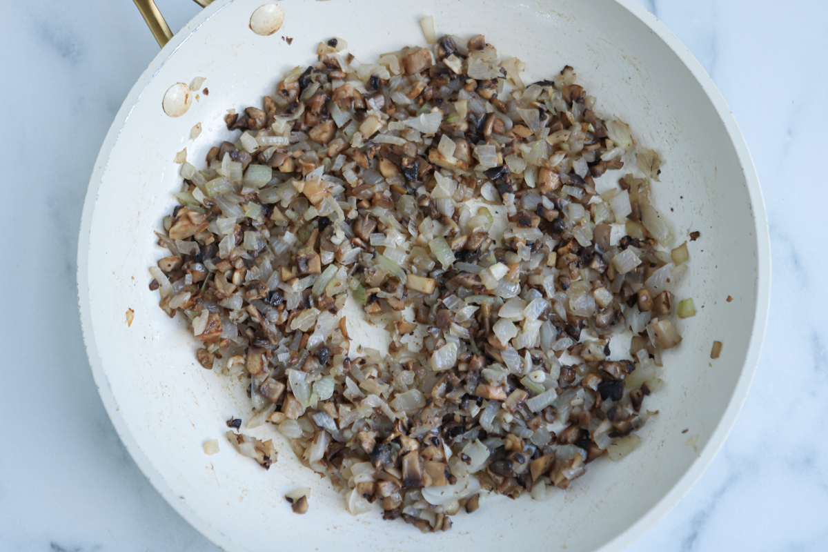 A white skillet contains finely chopped onions and mushrooms, sautéed until soft and slightly browned—the perfect savory base for kotlety mielone, spread evenly across the pan.