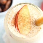 A refreshing peach yogurt smoothie topped with juicy peach slices and cinnamon, served with a bamboo straw. Text above: Easy Healthy Peach Yogurt Smoothie. Visit www.hollytasteful.com for the full recipe!.