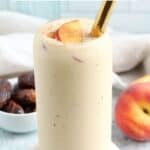 A tall glass of peach yogurt smoothie with a gold straw, garnished with peach slices. Beside the glass are a fresh peach and dates. Text on the image highlights 5-Minute Healthy Peach Yogurt Smoothie.