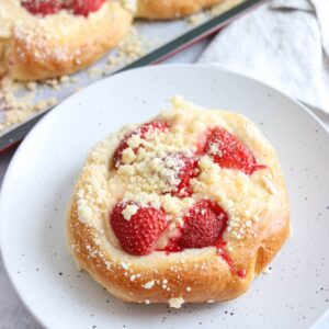 A round pastry topped with sliced strawberries and crumbly streusel sits on a white speckled plate.