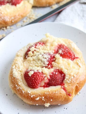 A round pastry topped with sliced strawberries and crumbly streusel sits on a white speckled plate.