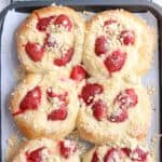 Six round Polish yeast buns topped with strawberries and pudding, arranged on a baking tray lined with parchment paper. While these sweet treats may differ from classic savory dishes like chicken parm meatballs, they share the same golden brown finish and tempting aroma fresh from the oven. Each bun has a crumbly topping for added texture and flavor.