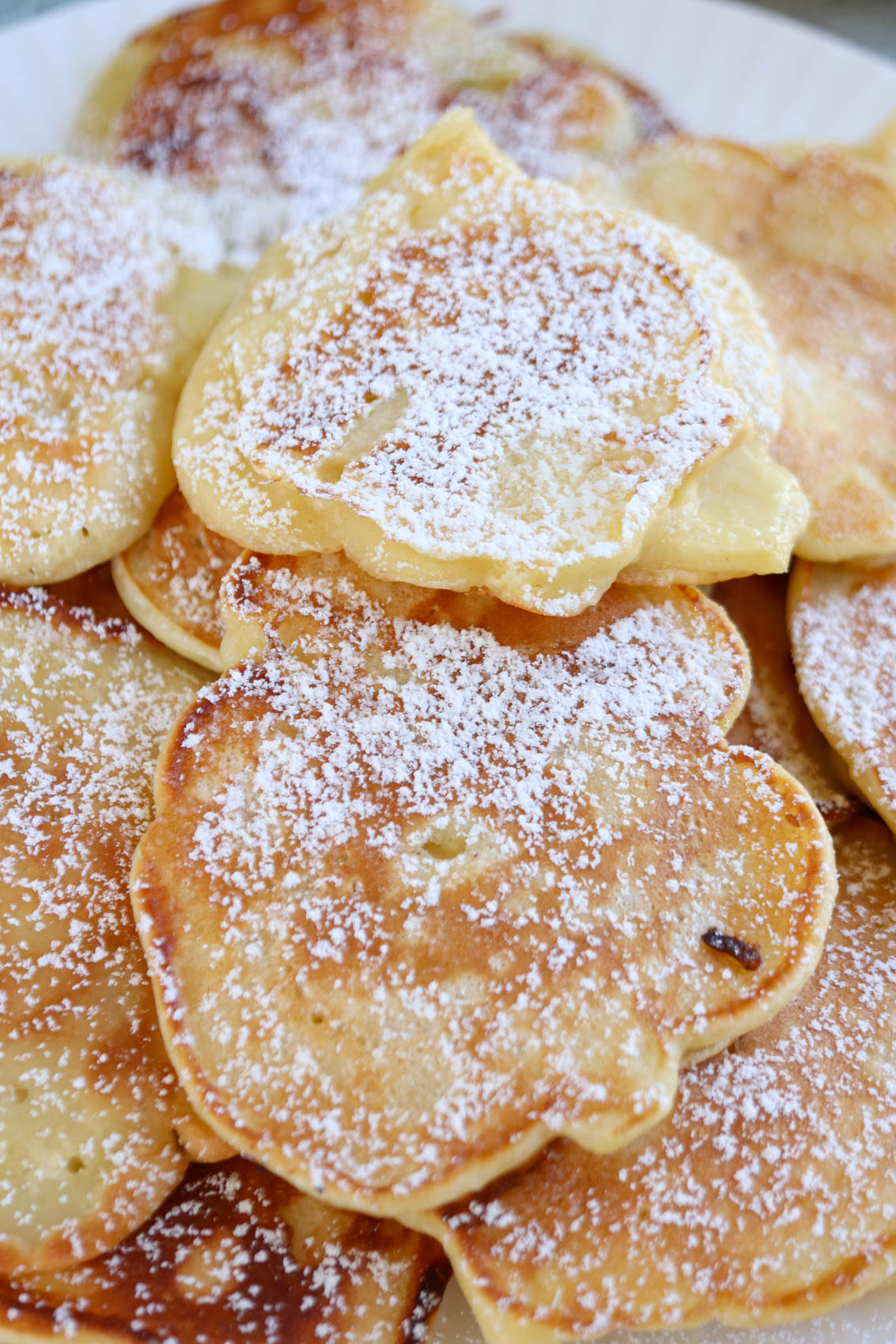 A close-up of golden brown Polish apple pancakes stacked on a plate, generously dusted with powdered sugar.