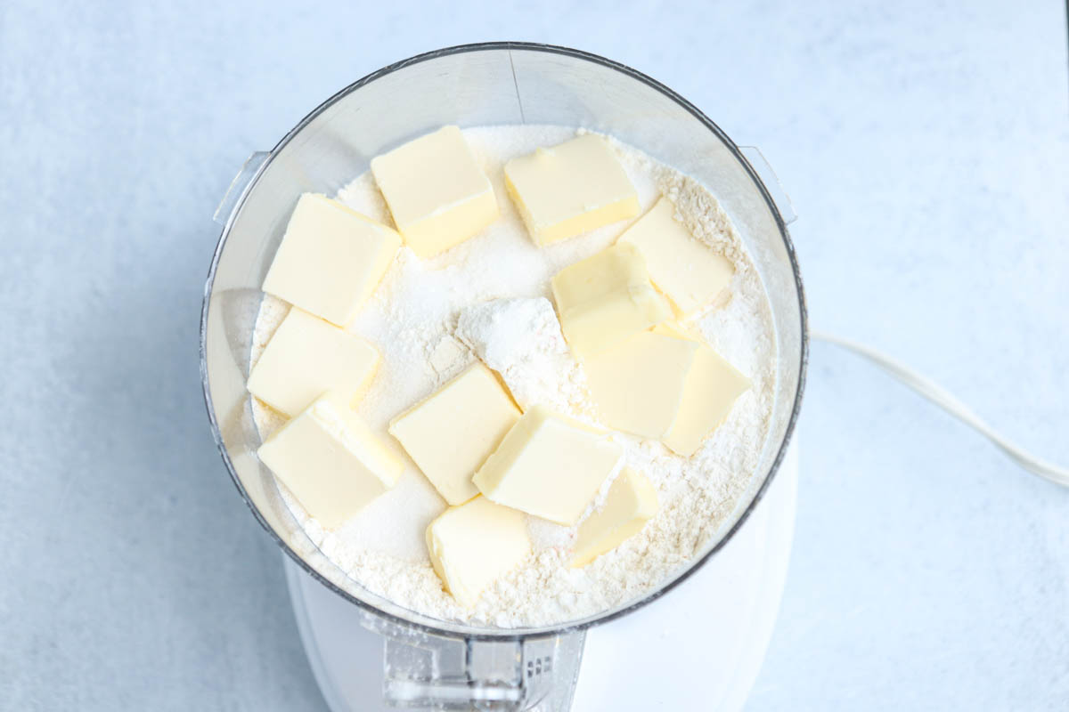 Cubes of butter on top of flour in a food processor, viewed from above, ready to be mixed for baking a classic Polish apple pie.