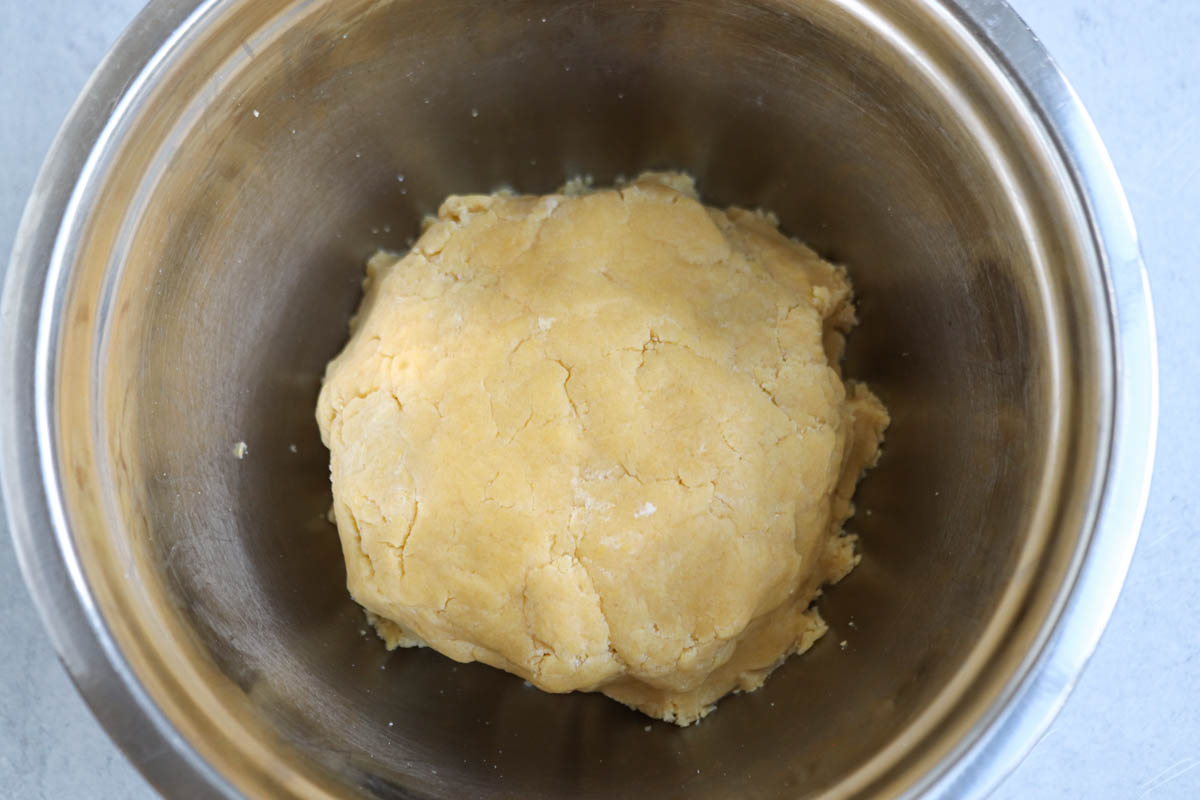 A ball of cookie dough sits in the center of a stainless steel mixing bowl on a light-colored surface, ready to be transformed into a delicious treat reminiscent of Polish apple pie.