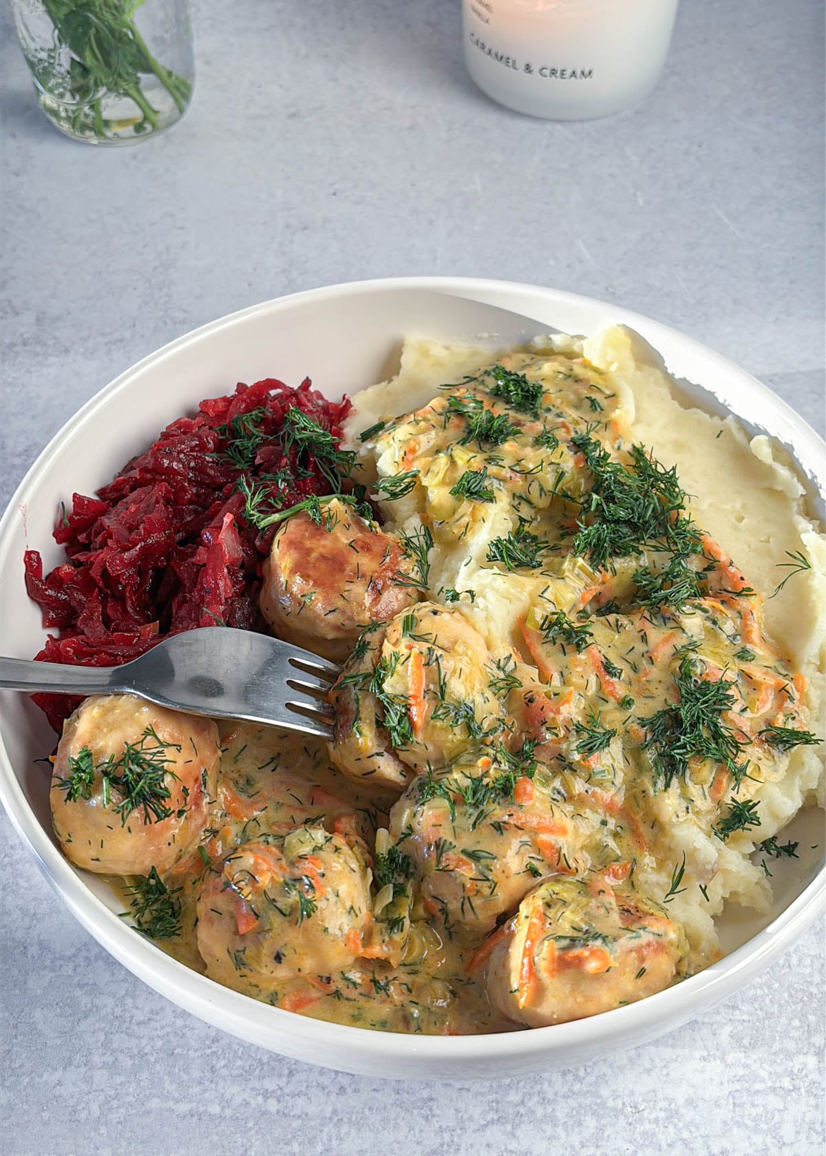 A bowl of Polish chicken meatballs in gravy served with mashed potatoes and shredded beets, topped with fresh dill.